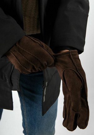 Bruine suède handschoenen met een gestructureerd oppervlak, voorzien van drie naadlijnen aan de achterkant. Draagt een persoon met een zwart jack.