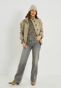 Veste beige en mélange de laine avec des boutons noirs, superposée à un haut imprimé léopard, associée à un jean flare gris et des bottines en daim beige.