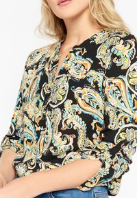 Svart skjorta med ett färgglatt paisleymönster i grönt, orange och blått. Har knäppning i halsen och rullade ärmar. Mjuk tygkvalitet.