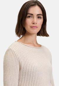 Helle beige Strickpullover mit geripptem Muster, weitem Ausschnitt und langen Ärmeln. Das Material wirkt weich und atmungsaktiv.