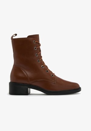 Botte chelsea en cuir marron avec laçage à l'avant, talon bloc bas noir et languette à l'arrière, vue de profil sur fond blanc.