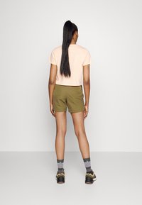 Camiseta corta de color rosa claro y pantalones cortos verdes oliva combinados con calcetines con patrón gris y verde y zapatillas deportivas oscuras, vista desde atrás.