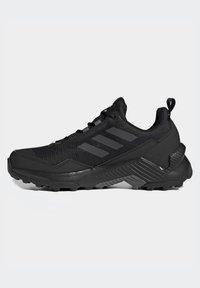 Chaussures de sport noires avec un dessus en tissu texturé, trois rayures foncées, un bout renforcé et une semelle en caoutchouc robuste pour une meilleure adhérence.