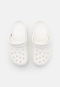 Paire de sabots blancs sans lacets avec des trous de ventilation et des sangles de talon réglables, vus de dessus sur fond blanc.