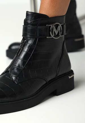 Bottines en cuir noir avec texture crocodile, dotées d'une fermeture éclair sur le côté et d'une boucle logo en argent. La semelle épaisse ajoute de la stabilité.