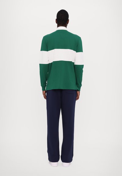 Grön långärmad skjorta med vita horisontella ränder, ribbad krage, i kombination med marinblå byxor. Tyget ser slätt och lätt ut.