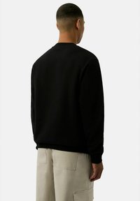 Felpa nera a girocollo con maniche lunghe, in tessuto misto cotone e con polsini a costine, indossata con pantaloni cargo beige chiaro.