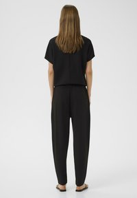 Schwarzes zweiteiliges Outfit mit einem kurzärmeligen Oberteil und locker sitzenden Hosen. Der Stoff wirkt weich mit einer glatten Textur und minimalen Details.