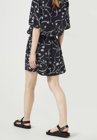 Svart klänning med vitt blommönster, korta ärmar, åtstramad midja, flödande tyg. Matchat med svarta platta sandaler.