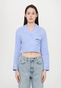 Zkrácená modro-bílá pruhovaná košile s dlouhými rukávy, zapínáním na knoflíky a kapsou se znakem "Moschino". Materiál z bavlny s lemováním.