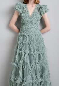 Robe vert menthe avec des couches à volants, des détails transparents, un décolleté en V et des manches ballon. Le tissu texturé présente des motifs en forme de cœur.