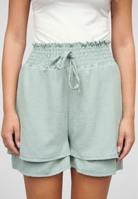 Lys grønne, teksturerte shorts med smocket midjebånd og justerbart bånd. Har lagdelt design som gir en løs og avslappet passform.