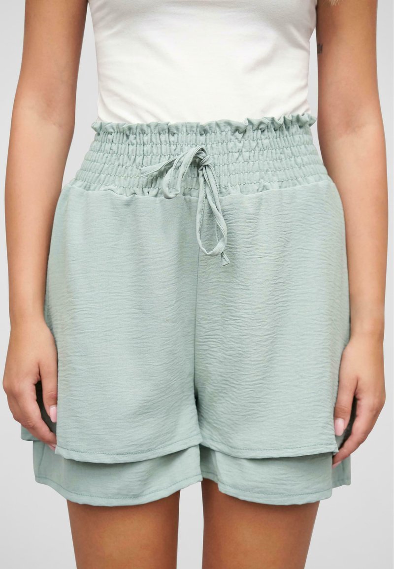 Lys grønne, teksturerte shorts med smocket midjebånd og justerbart bånd. Har lagdelt design som gir en løs og avslappet passform.