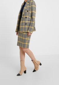 Dvojřadý plaid blazer v černé a žluté barvě s odpovídající sukní. Béžové kotníkové boty s špičatými černými špičkami a detaily knoflíků.