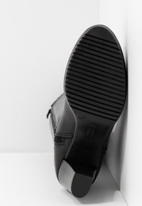 Semelle de bottine noire à cheville avec des rainures horizontales, taille 37, et un petit talon carré sur un fond blanc en coin.