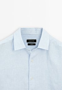 Camicia di lino azzurro chiaro con righe bianche verticali, colletto abbottonato e due bottoni sulla patta. L'etichetta dice "Massimo Dutti."