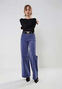 Pantalones de pana morados de pierna ancha con una textura suave, combinados con una camiseta de manga larga negra con canalé y una hebilla de cinturón en forma de corazón.