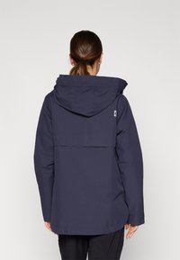 Veste imperméable bleu marine avec capuche, présentant un design de liège arrière et un logo sur l'épaule gauche. Fini lisse et mat avec une coupe décontractée.