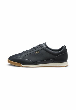 Czarny niski skórzany sneaker z beżową podeszwą, zaokrąglonym noskiem, sznurowaniem z przodu oraz małym złotym logo "BOSS" na bocznej części.