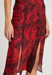 Röd och svart ormtryck klänning med två frontslitsar. Tillverkad av ett mjukt tyg, med en figurnära design och texturerat mönster.