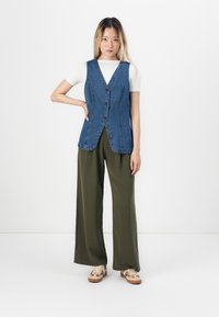 Jeansvest med v-hals og knapper, sammen med løse olivenbukser og mønstrede sneakers. Glat tekstur, afslappet design.