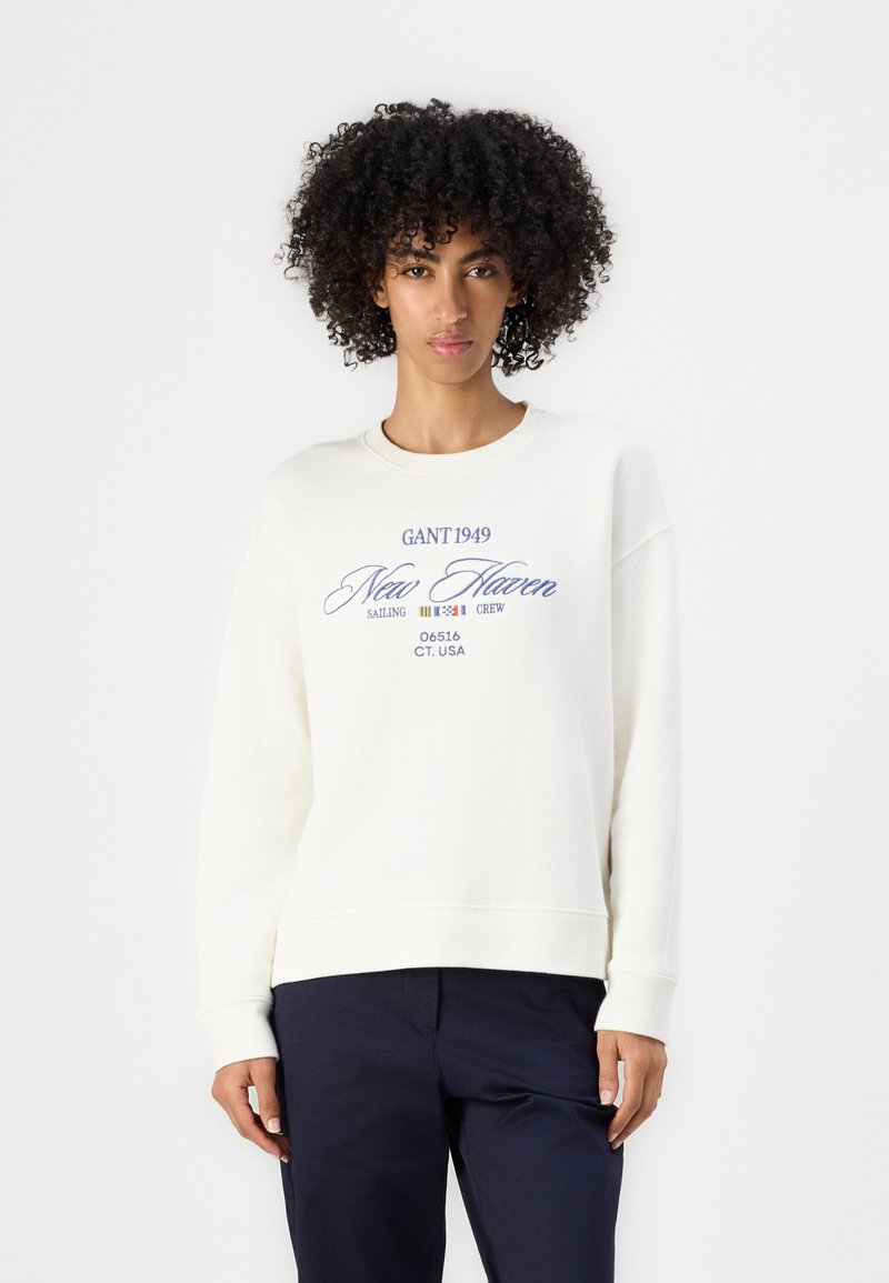 Sweatshirt couleur crème en coton doux, avec du texte violet qui indique "GANT 1949 New Haven Sailing Crew 06516 CT. USA."