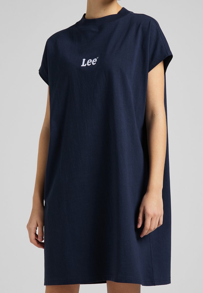 Robe sans manches bleu marine avec petit logo "Lee" sur la poitrine, portée par une personne en posture détendue devant un fond uni.