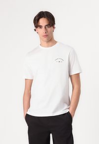 Biely bavlnený tričko s okrúhlym výstrihom, na prednej strane s malým vyšitou logom "Tommy Hilfiger" v tmavočervenej farbe na hrudi. Kombinované s čiernymi nohavicami.