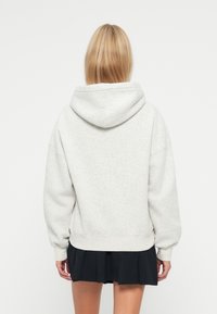 Felpa con cappuccio grigia realizzata in morbido tessuto, con vestibilità comoda e polsini e orlo a costine, abbinata a una gonna pieghettata nera.