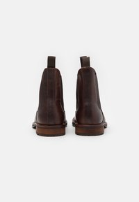 Botas Chelsea de cuero marrón con paneles elásticos laterales, un acabado texturizado y suelas de madera marrón. Con pestañas en la parte trasera para facilitar su uso.