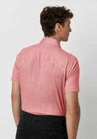 Kortebloes met kraag in het roze, gemaakt van een gestructureerde stof, met een rugnaad en een getailleerde pasvorm. Gecombineerd met zwarte broek.