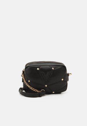 Sac bandoulière matelassé noir avec clous dorés, détail chaîne dorée et fermeture éclair sur le dessus, sur un fond uni.