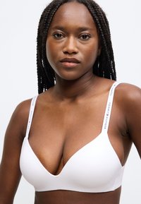 Λευκό σουτιέν με τρίγωνο σχήμα και ομαλή υφή. Διαθέτει ρυθμιζόμενους ιμάντες με το λογότυπο "Tommy Hilfiger". Χωρίς επιπλέον διακοσμήσεις ή σχέδια.