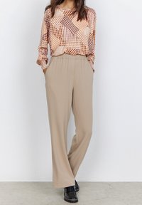 Long-sleeve top with a geometric pattern in warm tones; beige wide-leg trousers. Model wears black platform shoes. Neutral backdrop.