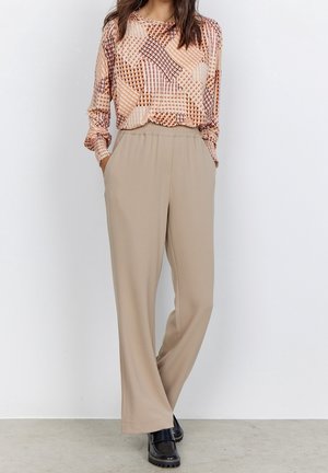 Long-sleeve top with a geometric pattern in warm tones; beige wide-leg trousers. Model wears black platform shoes. Neutral backdrop.
