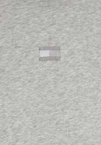 Petit rectangle brodé avec un carré blanc à gauche et des nuances de gris à droite sur un fond de tissu gris.