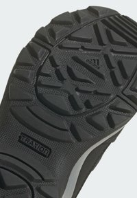 Semelle extérieure en caoutchouc noir avec une bande de roulement profonde conçue pour la traction ; comprend un marquage "TRAXION" et une surface texturée pour la durabilité.