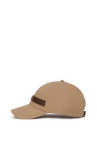 Tan baseball cap with a wide curved brim, textured fabric, brown leather accent band, and metallic logo detail on the side.