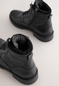 Schwarze Leder-Stiefeletten mit strukturierter Oberfläche, ausgestattet mit einem Reißverschluss, weichem Innenfutter und einer dicken Gummisohle.