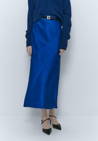 Sininen satiininen midi-hame, jossa on sileä pinta, istuva vyötärö ja musta vyö. Yhdistetty mustiin teräväkärkisiin korkokenkiin.