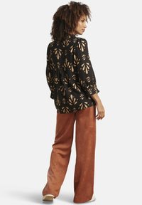 Black blouse with floral gold patterns, loose fit, and puff sleeves, paired with rust-colored wide-leg trousers in soft fabric.