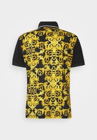 Polo noir à manches courtes avec un motif baroque doré complexe et le texte « Versace Jeans Couture » au dos.