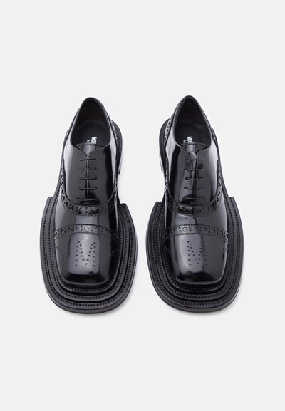 Μαύρα γυαλιστερά δερμάτινα παπούτσια με κορδόνια, τετράγωνα δάχτυλα και παχιά, στρωματοποιημένα πέλματα, με λεπτομέρειες περίεργων διατρήσεων τύπου brogue.