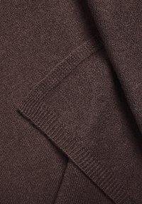 Brunt strikket stof med en blød tekstur, der har en ribkant og en let løs vævning, der viser sammenflettede fibre i hele stoffet.