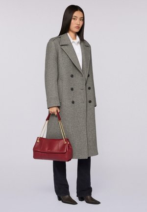 Abrigo de lana gris de doble botonadura, camisa blanca, pantalones negros, sosteniendo un bolso de cuero rojo con cadenas doradas y botas marrones de punta.