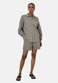 Conjunto de camisa de botones y pantalones cortos en verde oliva, con rayas verticales blancas, corte relajado y tejido ligero. Sandalias negras de dedo completan el look.
