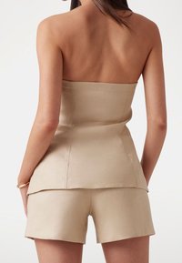 Top beige senza spalline con un design aderente, realizzato in un tessuto liscio, abbinato a pantaloni corti coordinati con un orlo semplice.