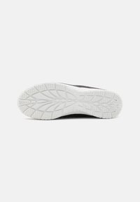 Suela de zapato atlético negro con una suela de goma blanca. Presenta un patrón de textura en la banda de rodadura para agarre y estabilidad.