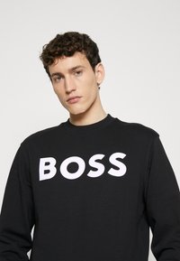 Sudadera negra de algodón con cuello redondo y gran logo blanco "BOSS" en la parte frontal. Textura suave con un corte relajado.