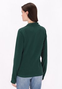 Pullover in pile verde scuro con maniche lunghe e colletto. Caratterizzato da una texture morbida e un design aderente che si adatta alla schiena.